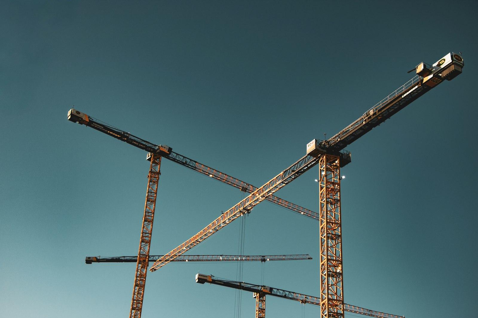 Tower cranes crossing against a clear evening sky